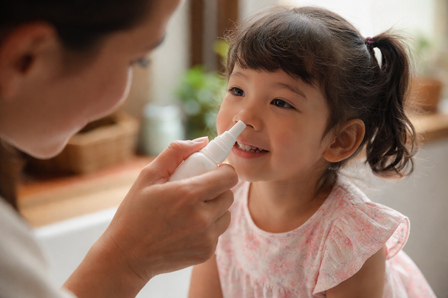 Una madre está rociando con un spray la nariz de su hija sonriente.